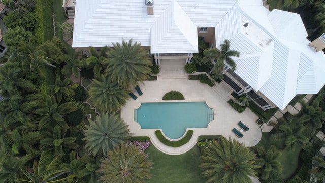 An aerial view of a house with white roof and beautiful swimming pool